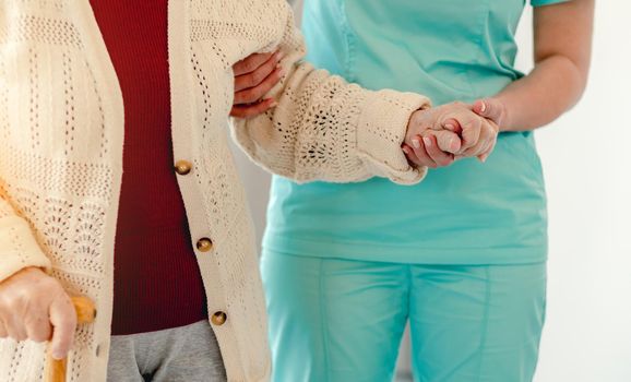 Close up view of old woman leaning on nurse while walking