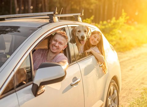 Father driving car with daughter and retriever dog on ground road at sunset