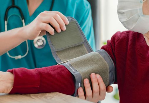 Doctor putting tonometer on old woman arm to measure blood pressure during appointment in quarantine period