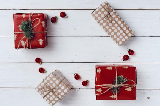 Packed small Christmas gifts and red baubles on white wooden board top view