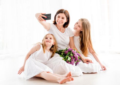 Happy mother with her pretty little girls making selfie. Daughters with mothers in white delicate dresses spending time together
