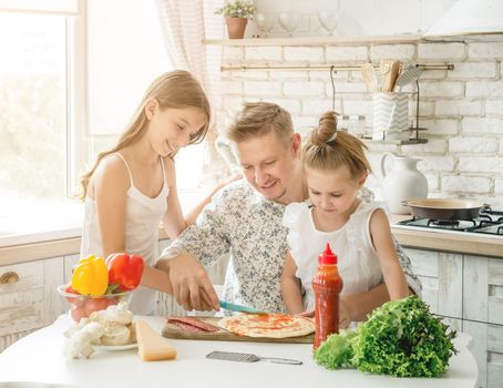 dad with two little daughters preparing pizza in the kitchen