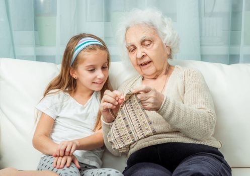 ganddaughter learning to embroider with granny on sofa