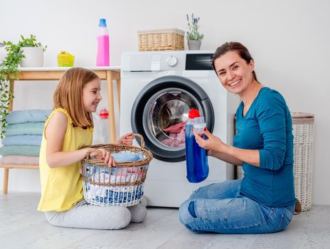 Happy mother and little daughter washing clothes using machine in light room