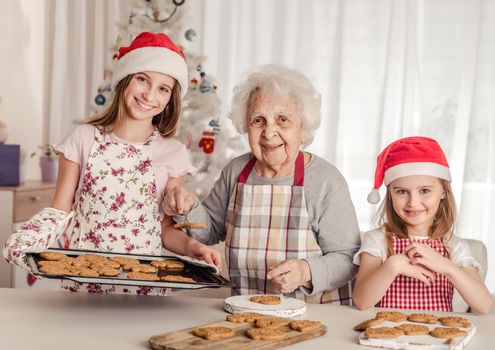 Grandmother with granddaughters in santa hats baking cookies