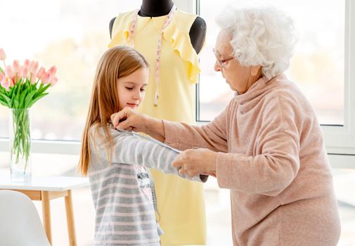 Senior lady measuring little model in sewing atelier