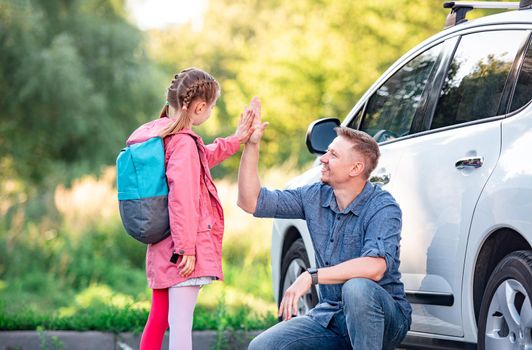 Little girl greeting father after school near car on sunny nature background