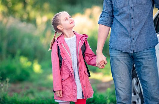 Little girl looking up on father before going to school on sunny nature background