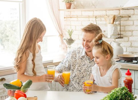 Dad with two daughters drinks orange juice in the kitchen