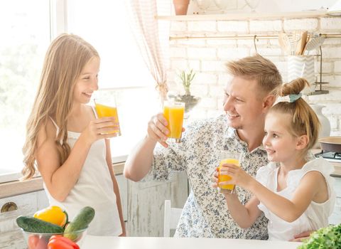 Dad with two daughters drinks orange juice in the kitchen