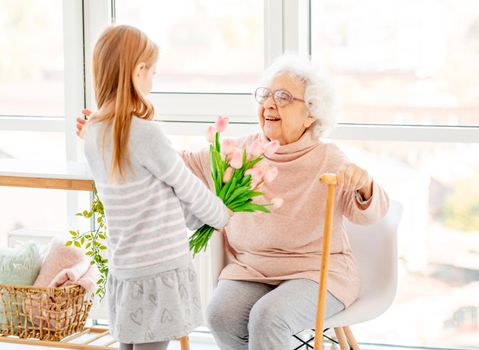 Nice little girl presenting bouquet to her grandmother in light room