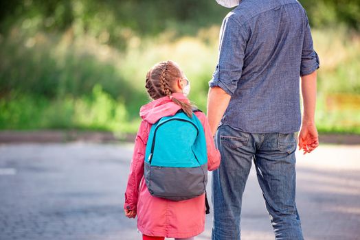 Rear view of little girl with backpack holding father's hand