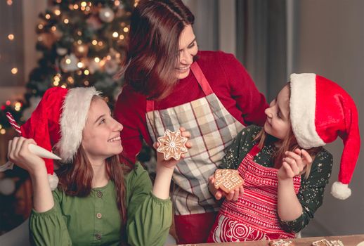 Smiling mother with daughters baking gingerbread near christmas tree at home