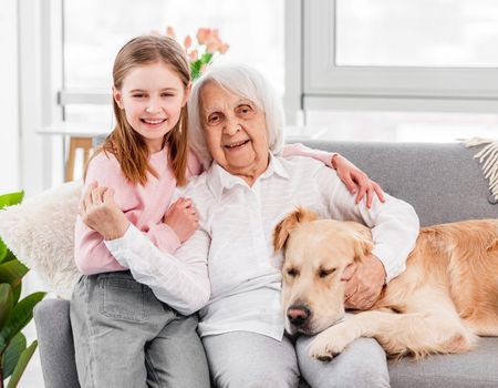Beautiful portrait of grandmother with granddaughter and golden retriever dog at home