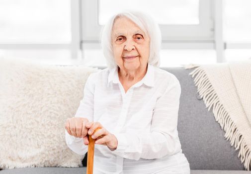 Portrait of elderly grey hair woman sitting at home and holding a wand and looking at the camera