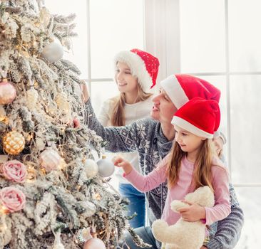 Father and daughters in santa hats decorating christmas tree