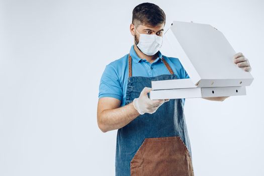 Pizza delivery man in medical gloves and mask against grey background. Safe service while coronavirus covid-19 outbreak