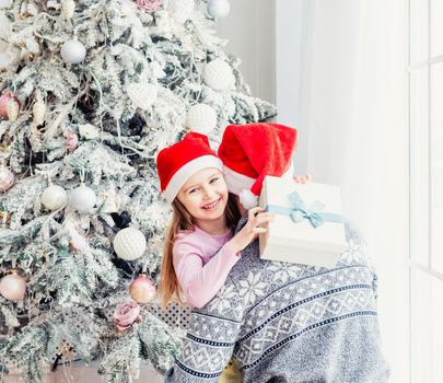 Little daughter in santa hat hugging father and holding gift