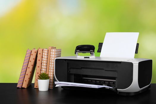 Compact home printer on desk with books against blurred background, close up