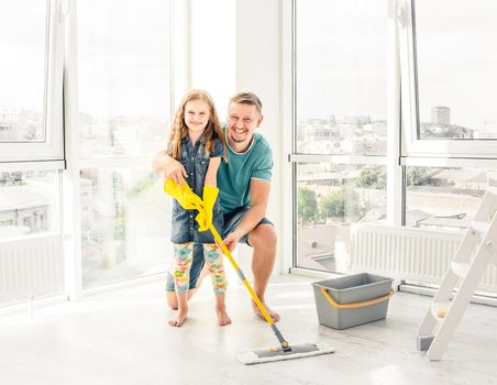 Little adorable girl helping her father to sweep the floor with soap water and mop
