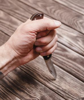 Man holding stainless jackknife on a wooden background, view of hand.