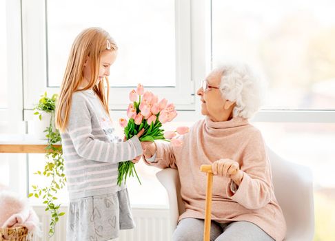 Nice little girl presenting bouquet to her grandmother in light room