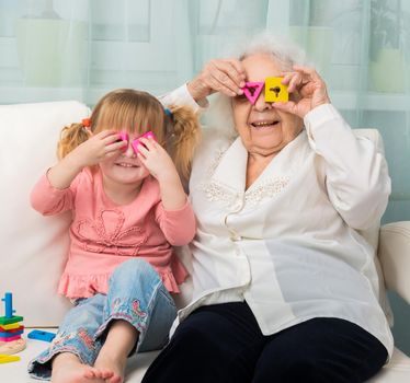 grandmother with granddaughter playing toys sitting on sofa