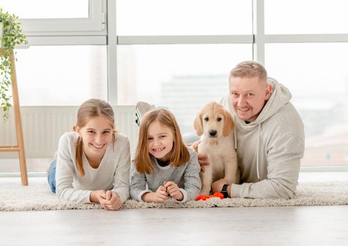 Smiling father with cute daughters and lovely puppy lying indoors