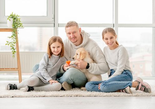 Happy family and golden retriever puppy sitting together indoors