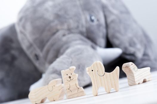 cute wooden toy animals on white wood plank with giant elephant doll in the background