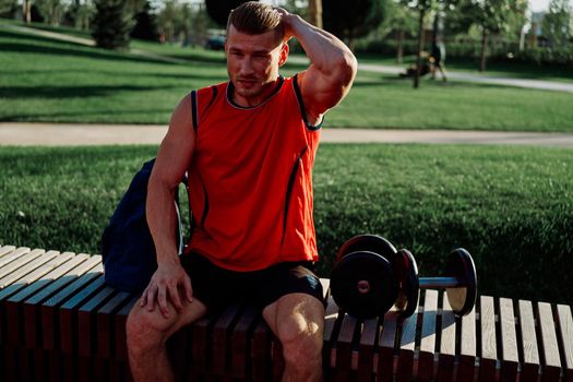 Cheerful male athlete in the park sits on a bench. High quality photo