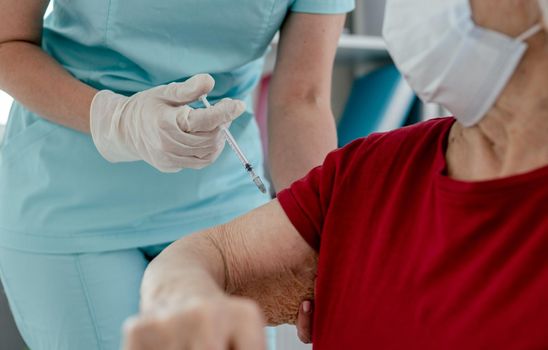 Nurse makes injection to elderly woman in mask during pandemic covid time. Healthcare worker girl cares about senior female person and did shot