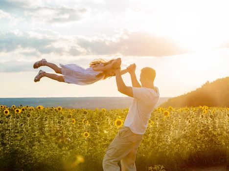 Dad playing with his daughter in a field at sunset