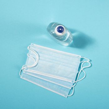 Alcohol gel hand sanitizer and disposable hygienic mask on blue background