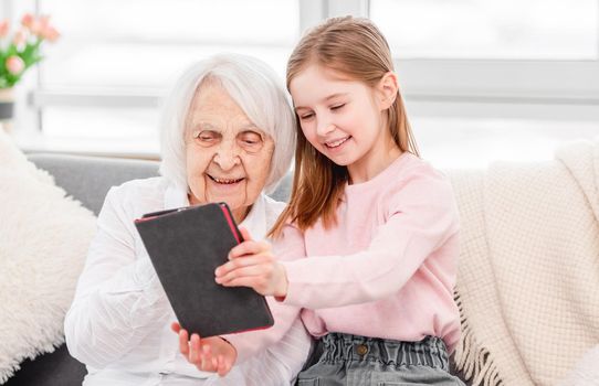 Portrait og grandmother and grandaughter with tablet at home. Elderly woman and young girl sitting and smiling