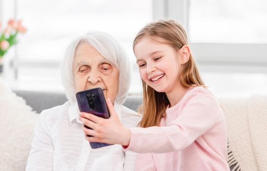 Granddaughetr making selfie on smartphone with her grandmother at home