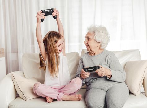 Smiling grandmother with little granddaughter playing games together with gamepads