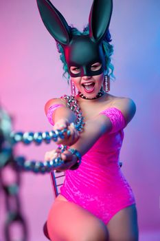 the woman in a bright pink bodysuit and rabbit mask poses against a bright background with a chain