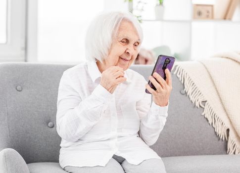 Modern ederly woman talking with friends by video using smartphone and smiling. Concept of old generation and new technologies