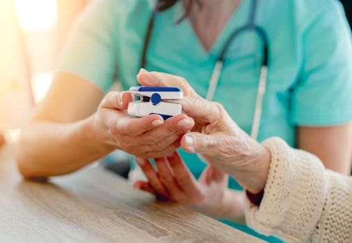 Doctor using pulse oximeter on old woman hand during appointment in clinic