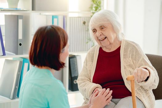 Old lady talking to caregiver holding hands in nursing home