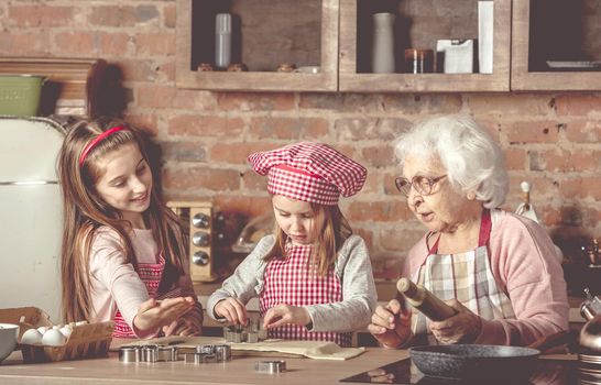 Two little granddaughters help granny to bake cookies at the rustic kitchen