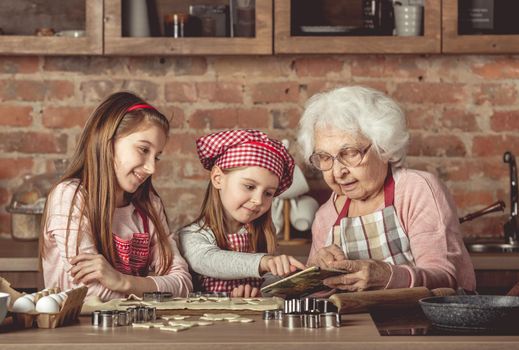 Grandma and granddaughters are spreading dough using a rolling pin