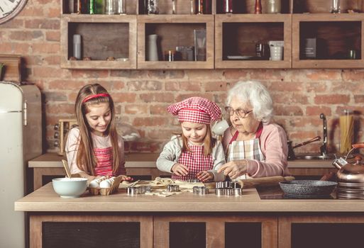 Two little granddaughters help granny to bake cookies at the rustic kitchen