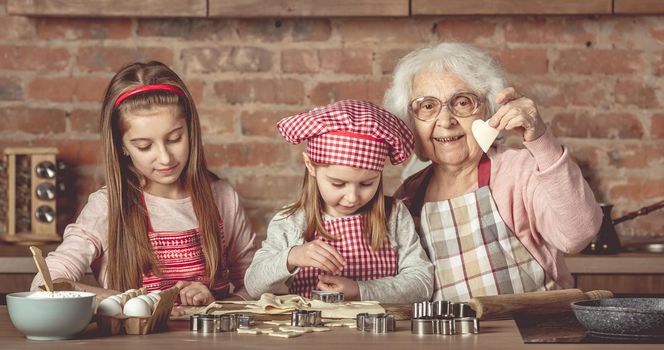 Two little girls making cookies with her granny at kitchen at home