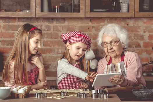 Grandma with her little granddaughters looking for a recipe using modern tablet