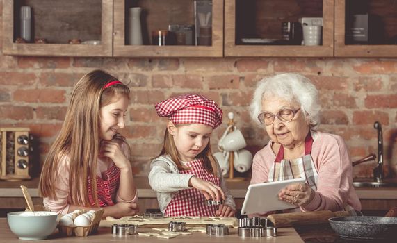 Grandma with her little granddaughters looking for a recipe using modern tablet