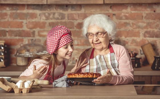 Little granddaughter with her senior granny enjoying the smell of hot homemade fruit pie