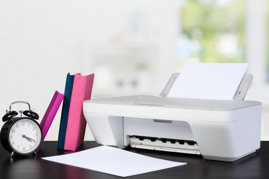 Compact home printer on desk with books against blurred background, close up
