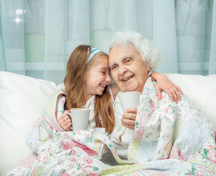 grandmother and granddaughter drink tea covered with blanket